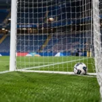 Een bal ligt net over de doellijn in een leeg doelgebied, met een Nations League-bord langs het veld.