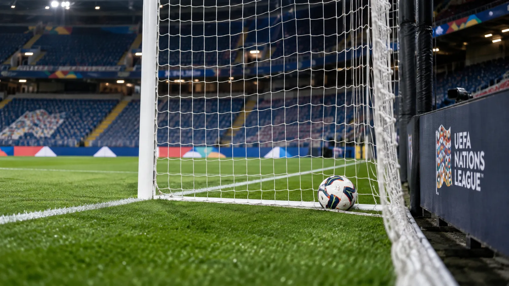 Een bal ligt net over de doellijn in een leeg doelgebied, met een Nations League-bord langs het veld.