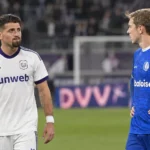 Twee voetballers van de tegenstanders praten na afloop op het veld.
