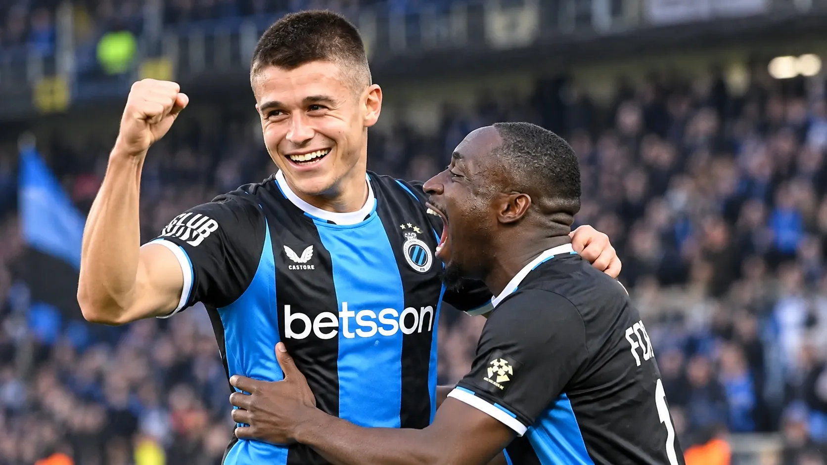 Twee spelers van Club Brugge vieren samen een doelpunt op het veld.