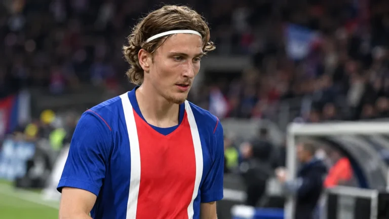 Een speler in een blauw-rood-wit wedstrijdshirt staat na een voetbalwedstrijd op het veld.