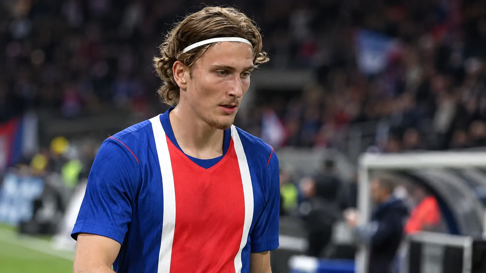 Een speler in een blauw-rood-wit wedstrijdshirt staat na een voetbalwedstrijd op het veld.