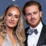 Twee formeel geklede gasten poseren bij een blauw decor van een voetbalgala.