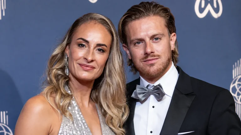 Twee formeel geklede gasten poseren bij een blauw decor van een voetbalgala.