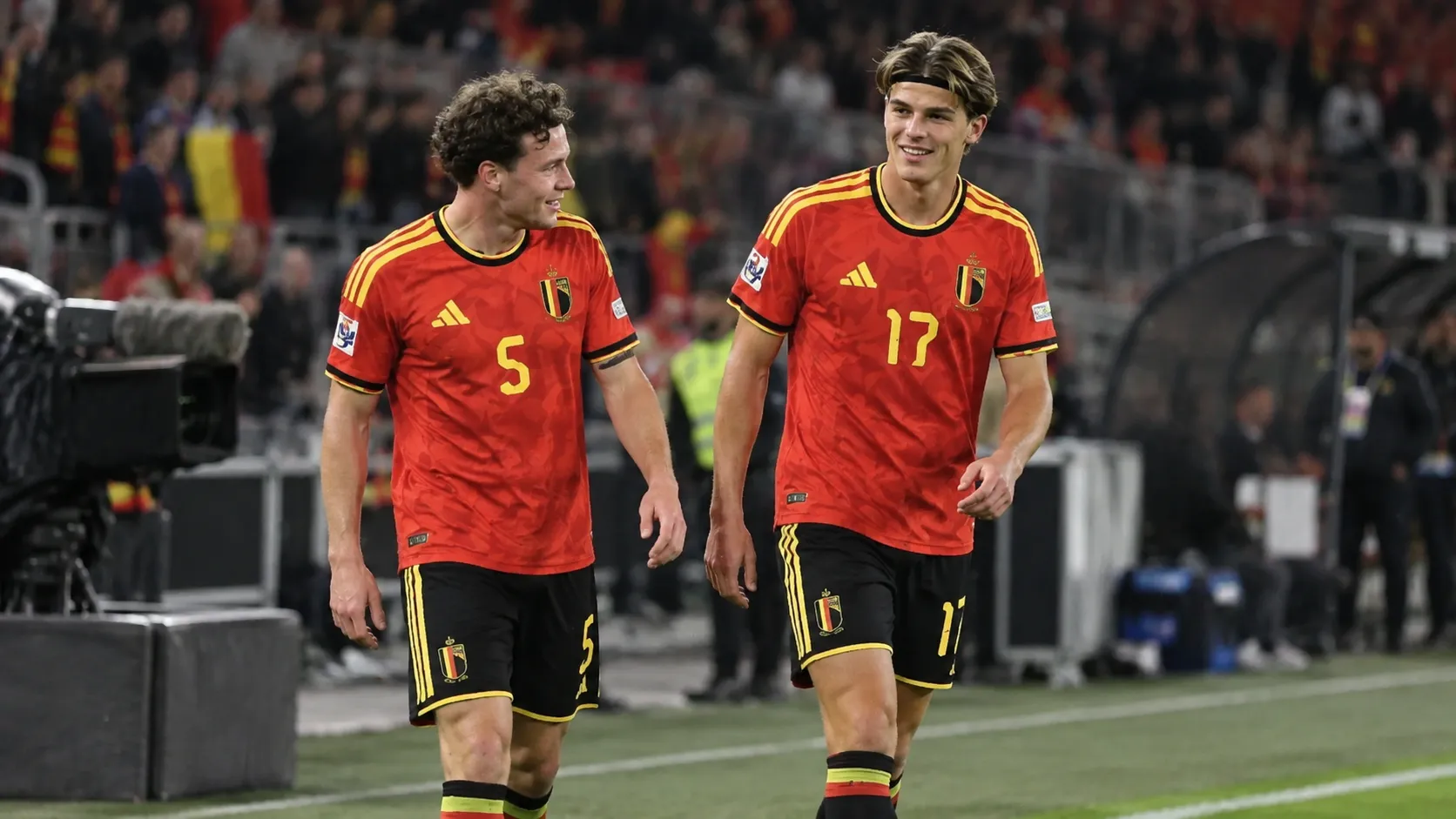 Twee Belgische internationals in rode shirts staan na een spelmoment aan de zijlijn.