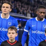 Twee spelers van KRC Genk staan met jeugdmascottes op het veld voor een wedstrijd.