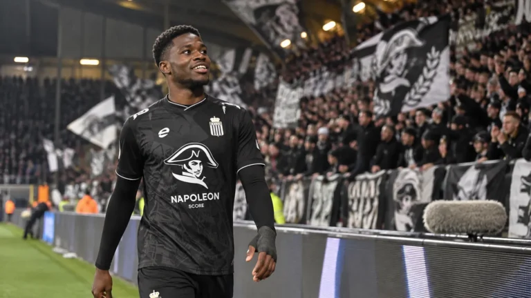 Cheick Keita in zwart voetbalshirt aan de rand van het veld voor een tribune.