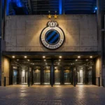 Verlichte ingang van een Club Brugge-stadioncomplex met het clubembleem boven de toegang.