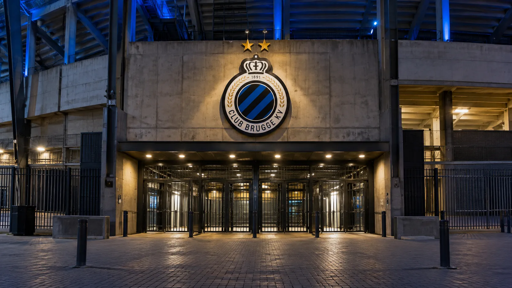 Verlichte ingang van een Club Brugge-stadioncomplex met het clubembleem boven de toegang.