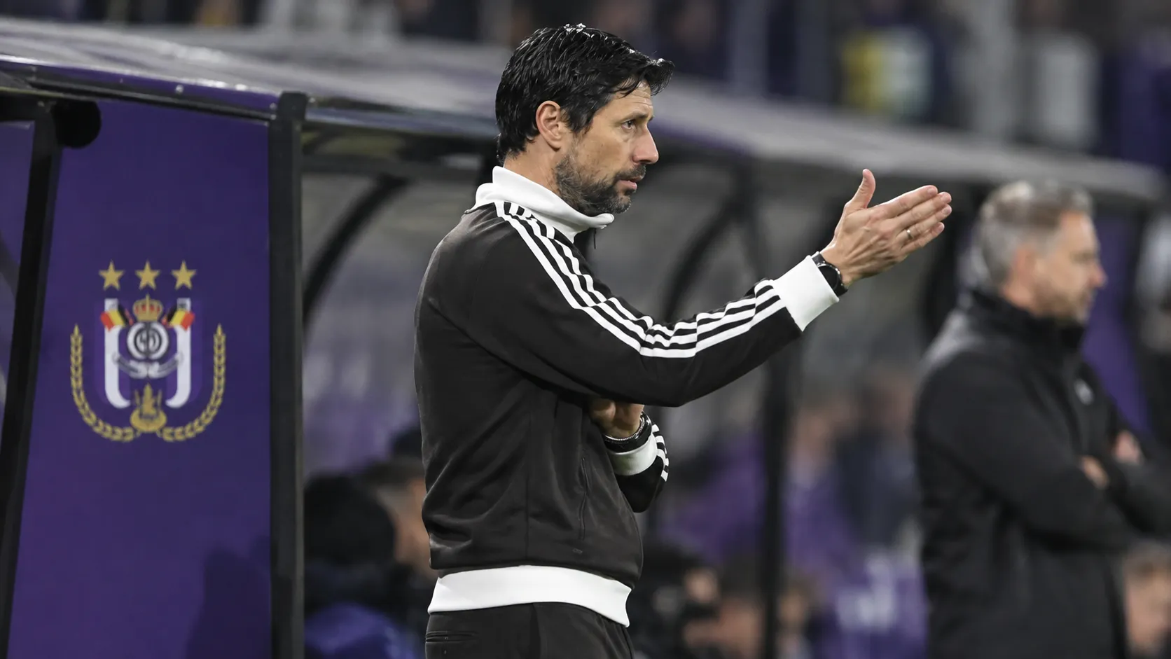 Vítor Bruno staat langs de zijlijn naast een paars dugoutpaneel van RSC Anderlecht.