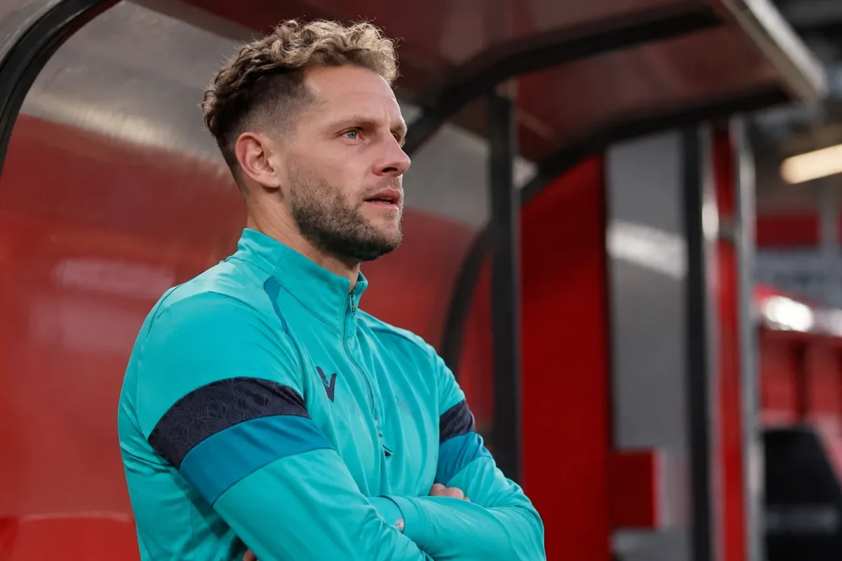 Mats Rits in een turquoise trainingsvest in een overdekte zone van een voetbalstadion.
