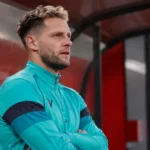Mats Rits in een turquoise trainingsvest in een overdekte zone van een voetbalstadion.
