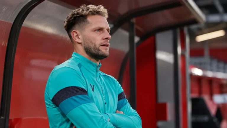 Mats Rits in een turquoise trainingsvest in een overdekte zone van een voetbalstadion.