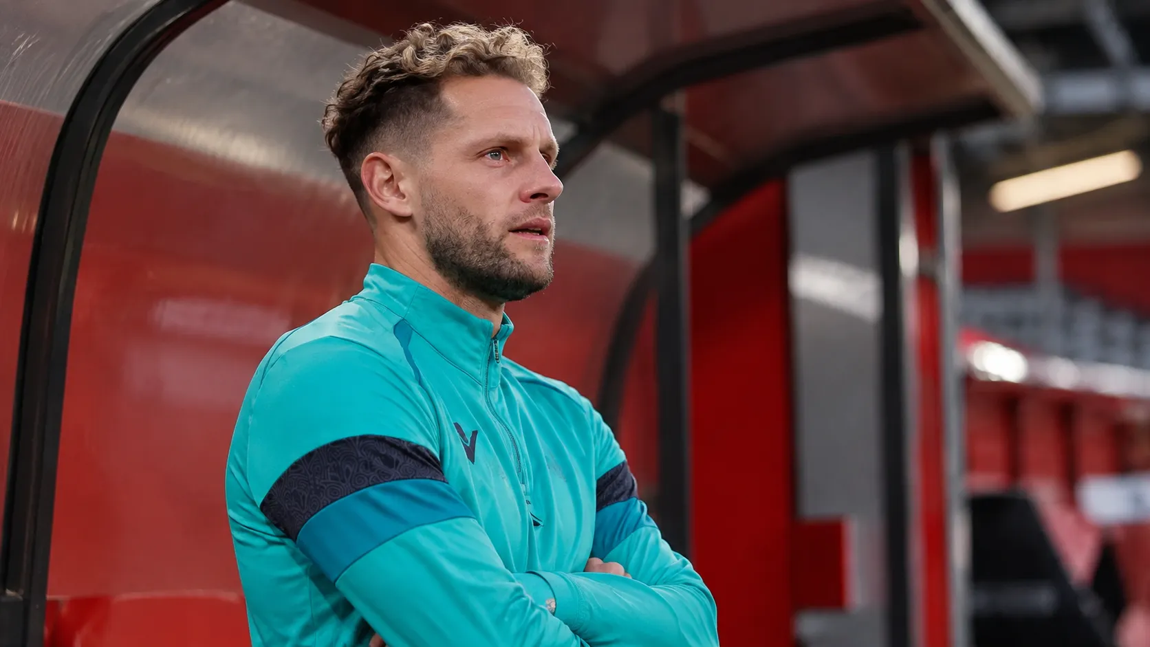 Mats Rits in een turquoise trainingsvest in een overdekte zone van een voetbalstadion.