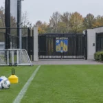Lege oefenzone aan het trainingscomplex van KVC Westerlo met een clubembleem op de toegangspoort.
