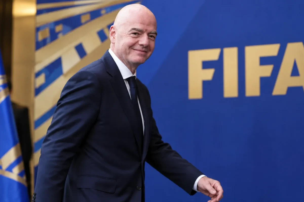 Gianni Infantino loopt in pak langs een FIFA-achtergrond.