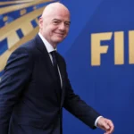 Gianni Infantino loopt in pak langs een FIFA-achtergrond.