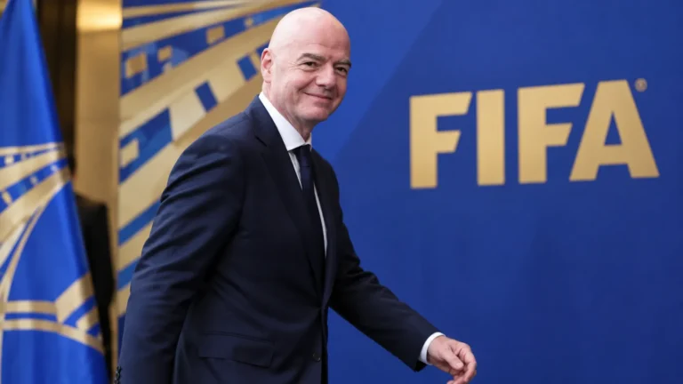 Gianni Infantino loopt in pak langs een FIFA-achtergrond.