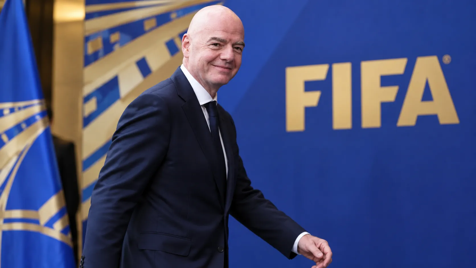 Gianni Infantino loopt in pak langs een FIFA-achtergrond.