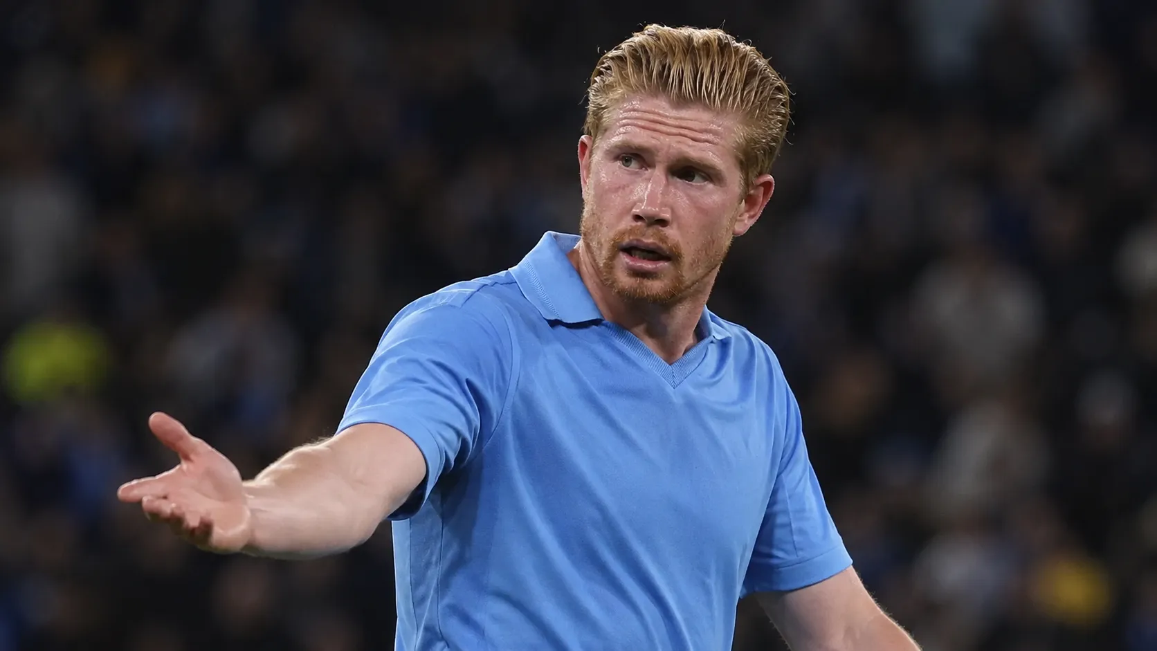 Kevin De Bruyne in een blauw Napoli-shirt kijkt tijdens een wedstrijd richting de zijlijn.