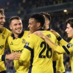 Een groep spelers in gele en donkerblauwe tenues verzamelt zich op het veld.