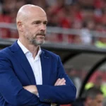 Erik ten Hag in een blauw pak aan de rand van een voetbalveld.