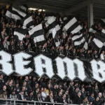 Een groep supporters van Sporting Charleroi zwaait met zwart-witte vlaggen in de tribune.