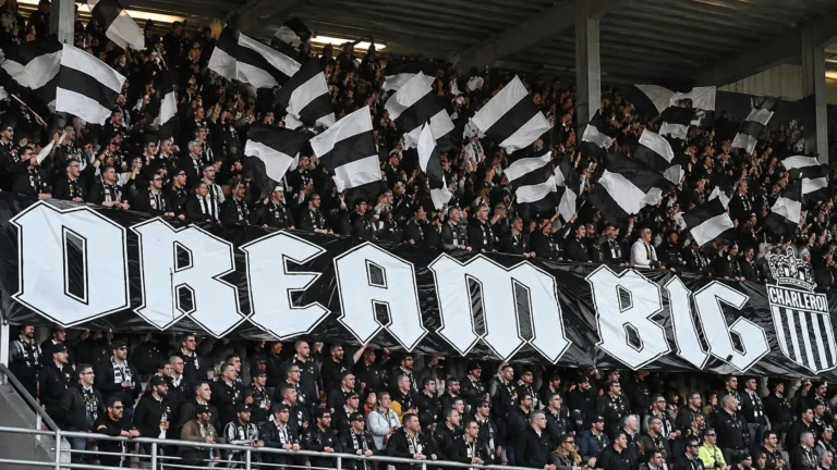 Een groep supporters van Sporting Charleroi zwaait met zwart-witte vlaggen in de tribune.