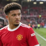 Jadon Sancho in zijn zichtbare bronshirt aan de rand van een voetbalveld.