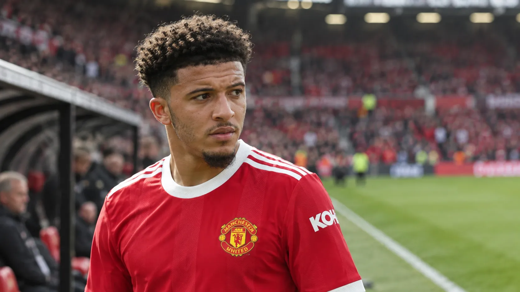 Jadon Sancho in zijn zichtbare bronshirt aan de rand van een voetbalveld.