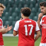Drie voetballers in rood-witte tenues tijdens een gezamenlijke opwarming in een stadion.