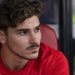 Julián Álvarez zit geconcentreerd op de reservebank in een stadion.