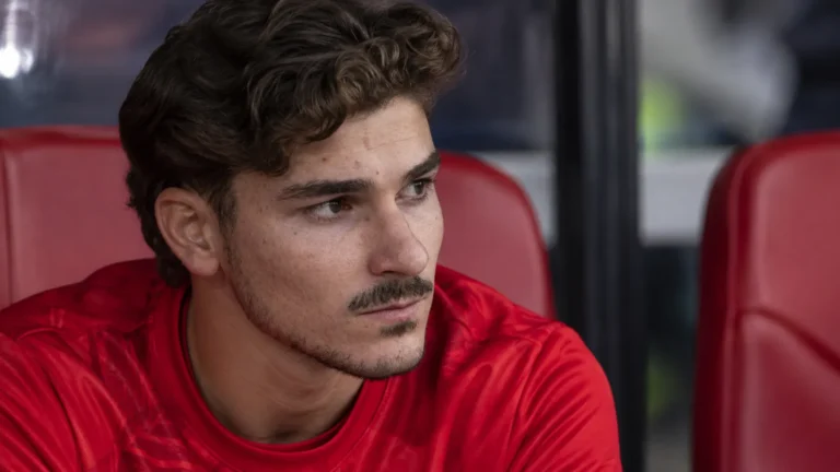 Julián Álvarez zit geconcentreerd op de reservebank in een stadion.