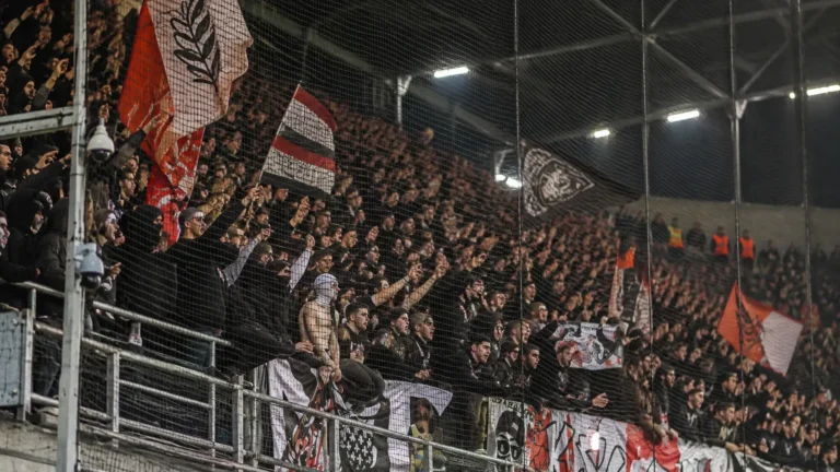 Een groep RC Lens-supporters achter een veiligheidsnet in een avondstadion.
