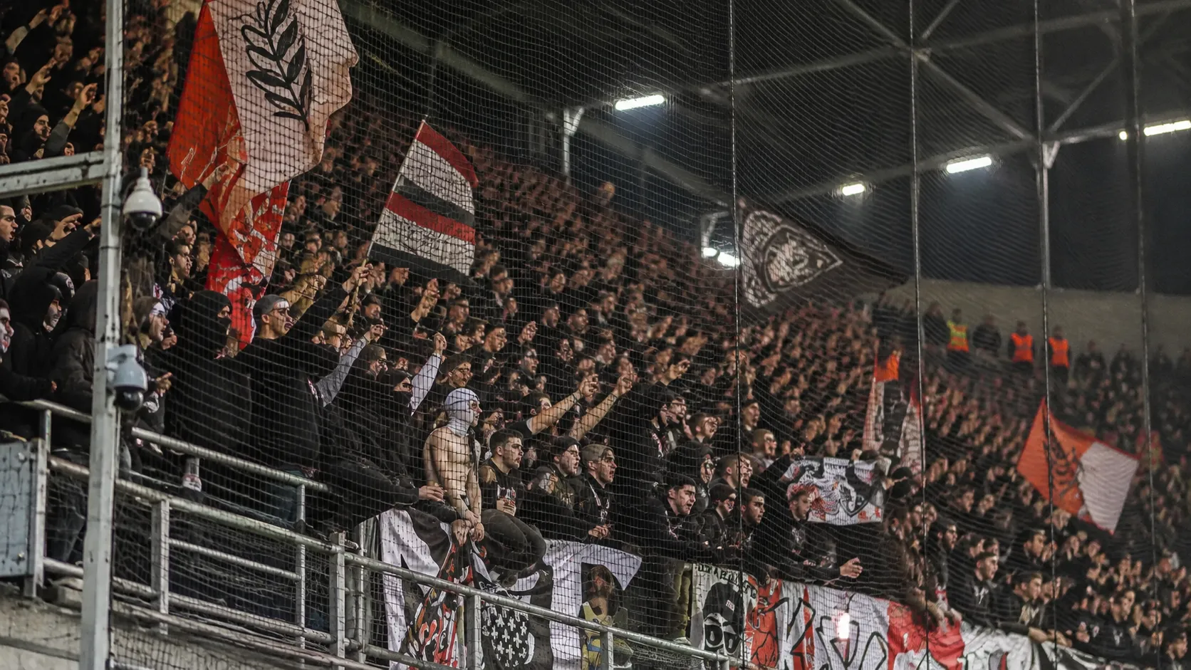 Een groep RC Lens-supporters achter een veiligheidsnet in een avondstadion.