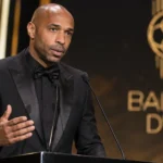 Thierry Henry spreekt op een Ballon d'Or-podium met een subtiel evenementsscherm op de achtergrond.