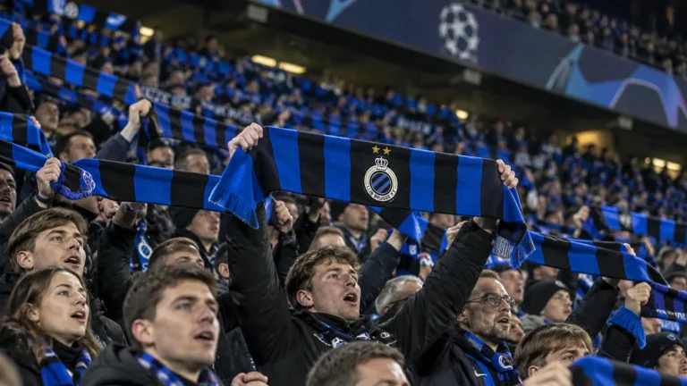 Collectieve Club Brugge-supporters met blauw-zwarte sjaals in een verlicht stadion.