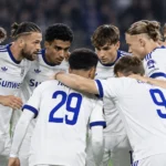 Een groep voetballers in witte tenues vormt een hechte huddle op het veld.