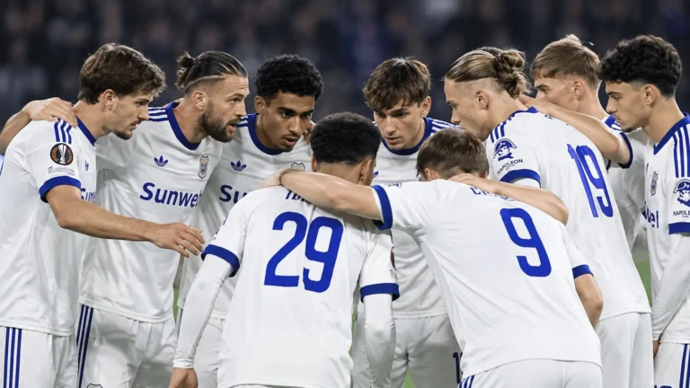Een groep voetballers in witte tenues vormt een hechte huddle op het veld.