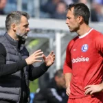 Een coach en een voetballer overleggen langs de zijlijn van een voetbalstadion.
