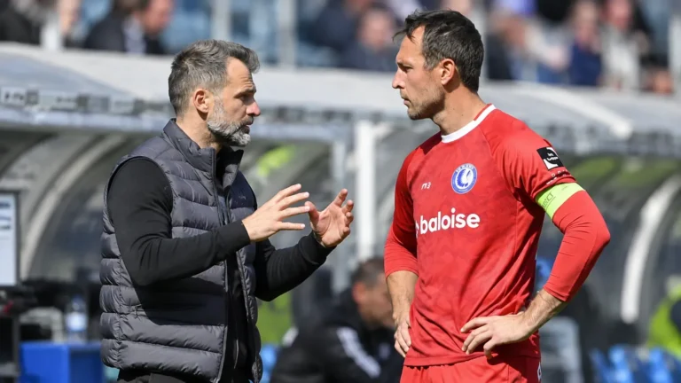 Een coach en een voetballer overleggen langs de zijlijn van een voetbalstadion.