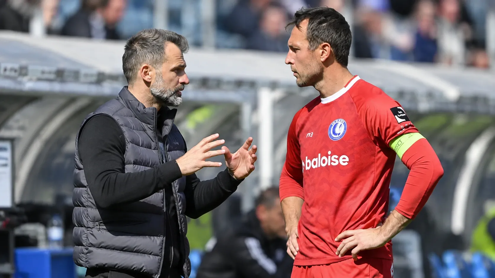 Een coach en een voetballer overleggen langs de zijlijn van een voetbalstadion.