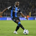 Carlos Forbs in het zwart-blauwe tenue van Club Brugge terwijl hij de bal controleert op een verlicht veld.