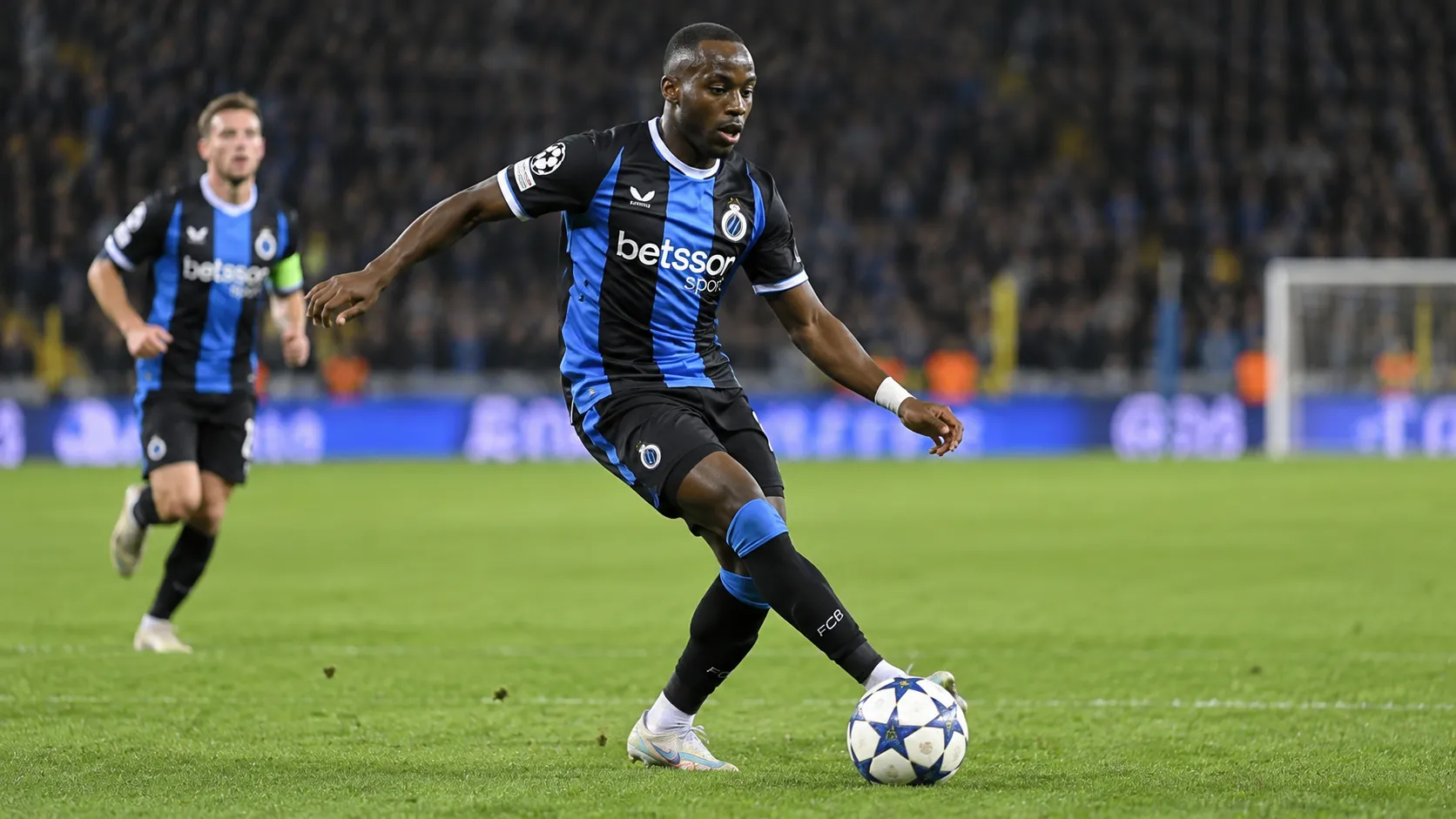 Carlos Forbs in het zwart-blauwe tenue van Club Brugge terwijl hij de bal controleert op een verlicht veld.