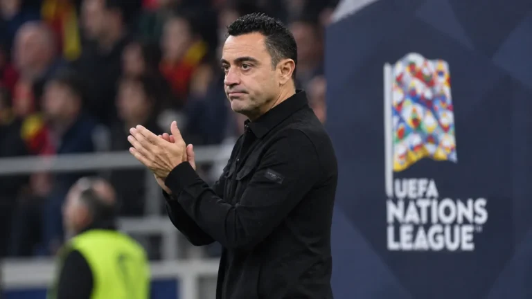 Een coach in donkere jas applaudisseert langs de zijlijn bij een Nations League-wedstrijd.