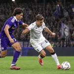 Twee voetballers in duel voor een volle tribune.