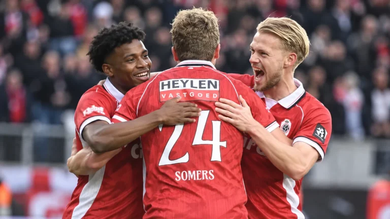 Een groep Antwerp-spelers in rode wedstrijdshirts viert samen op het veld.