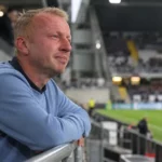 Sven Vandenbroeck staat in een stadion en kijkt bedachtzaam naast de camera.
