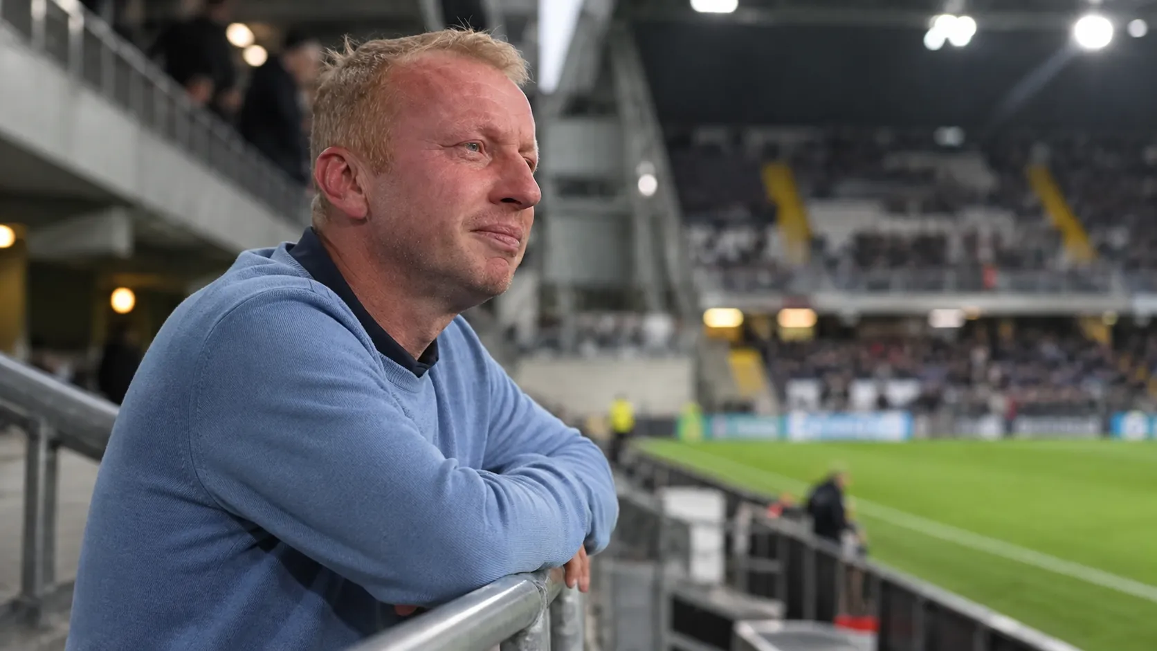 Sven Vandenbroeck staat in een stadion en kijkt bedachtzaam naast de camera.