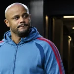 Vincent Kompany in een blauw sportjack bij de ingang van een voetbalstadion.